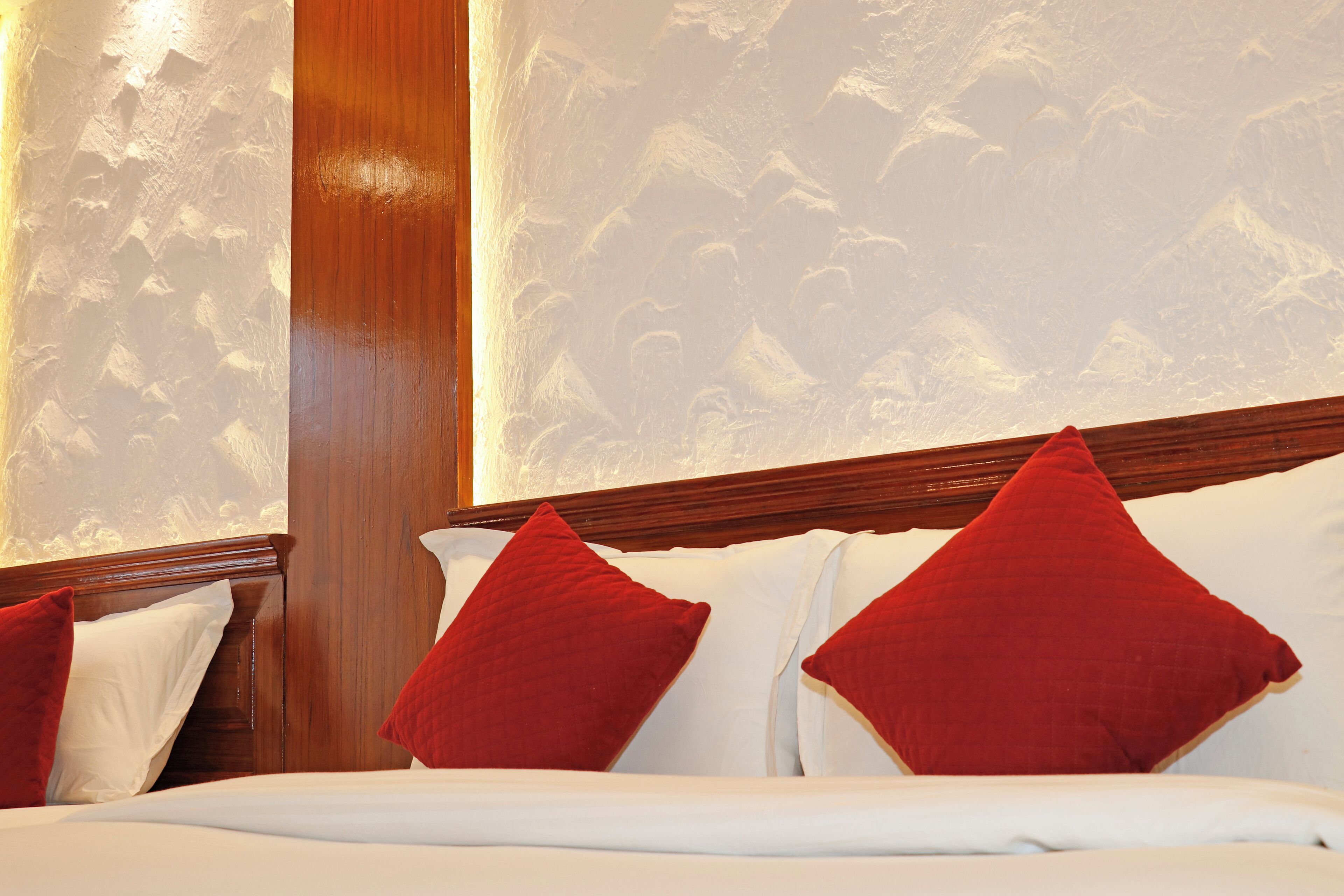 A hotel room with a wooden headboard, white bedding, and red pillows.
