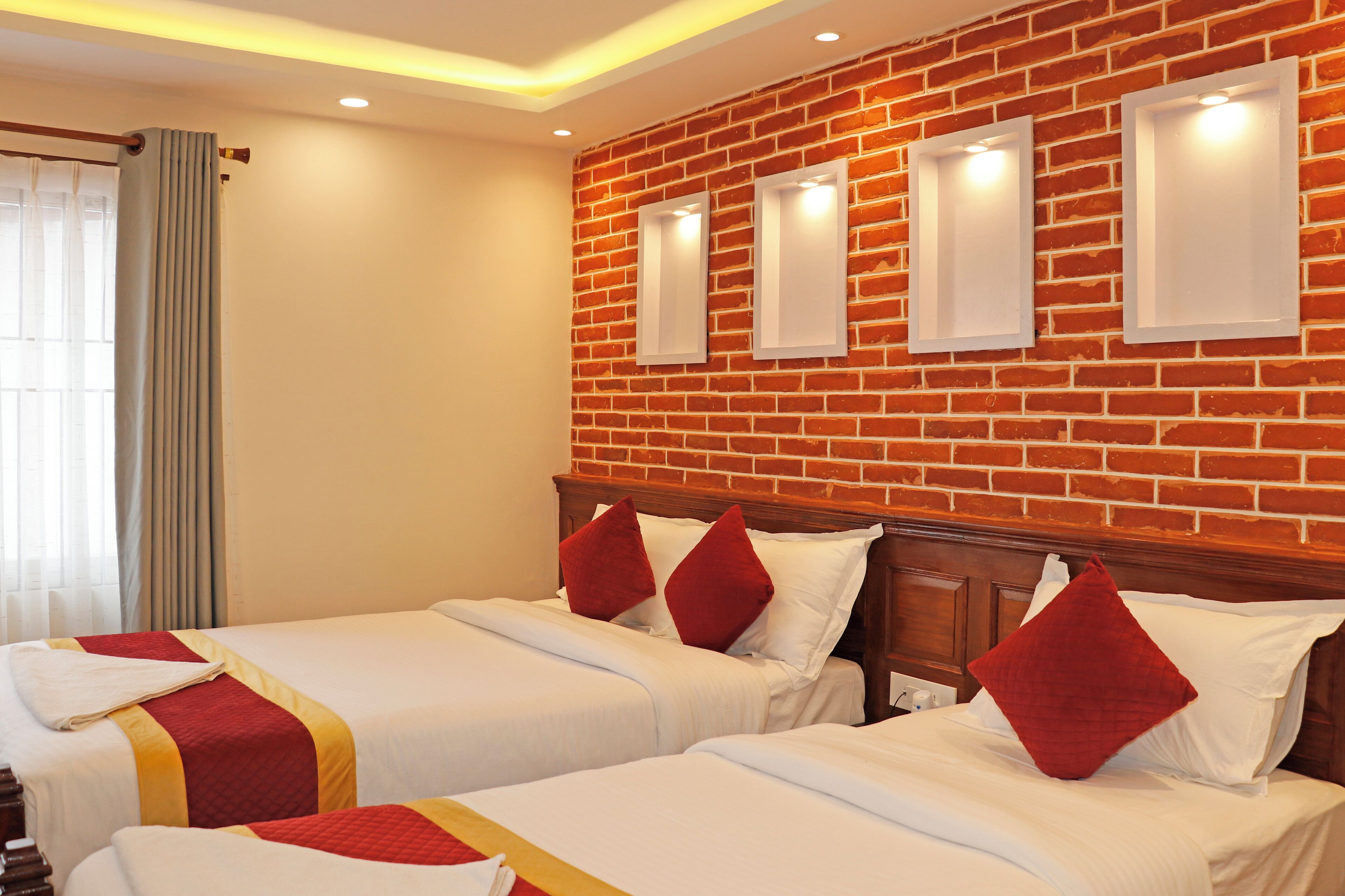 A hotel room with two beds, a brick wall, and recessed lighting.