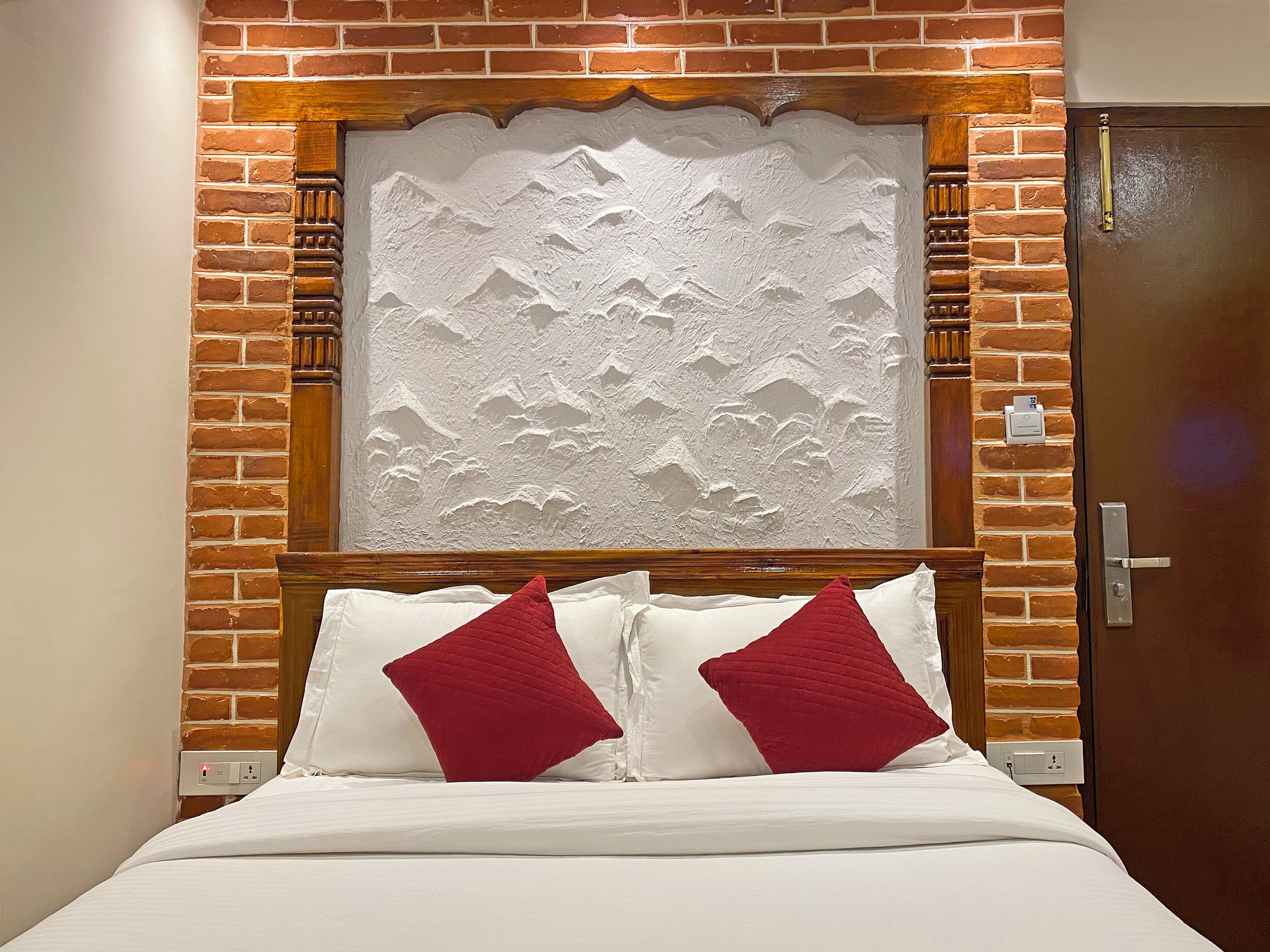 Ein Hotelzimmer mit Backsteinwand, Holzkopfstütze und einem Bett mit weißer Bettwäsche und roten Kissen.