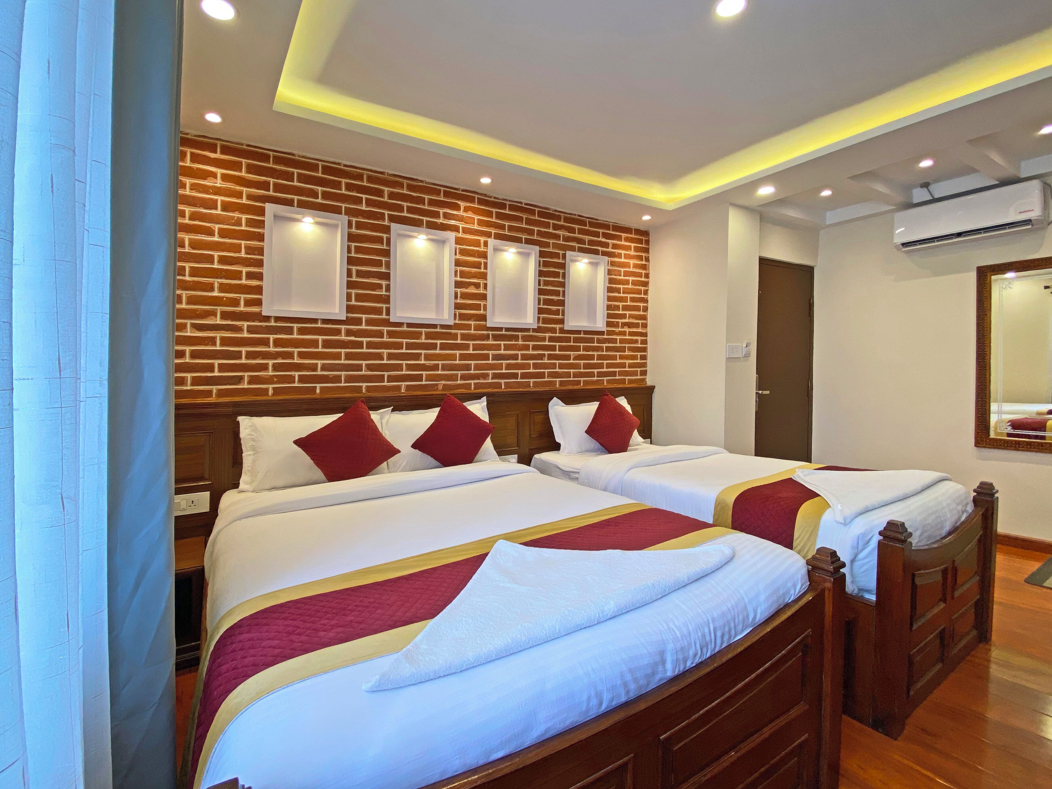A hotel room with two beds, a brick wall, recessed ceiling lights, and an air conditioning unit.