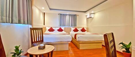 A hotel room with two beds, a small table, a chair, a potted plant, and a window with curtains.
