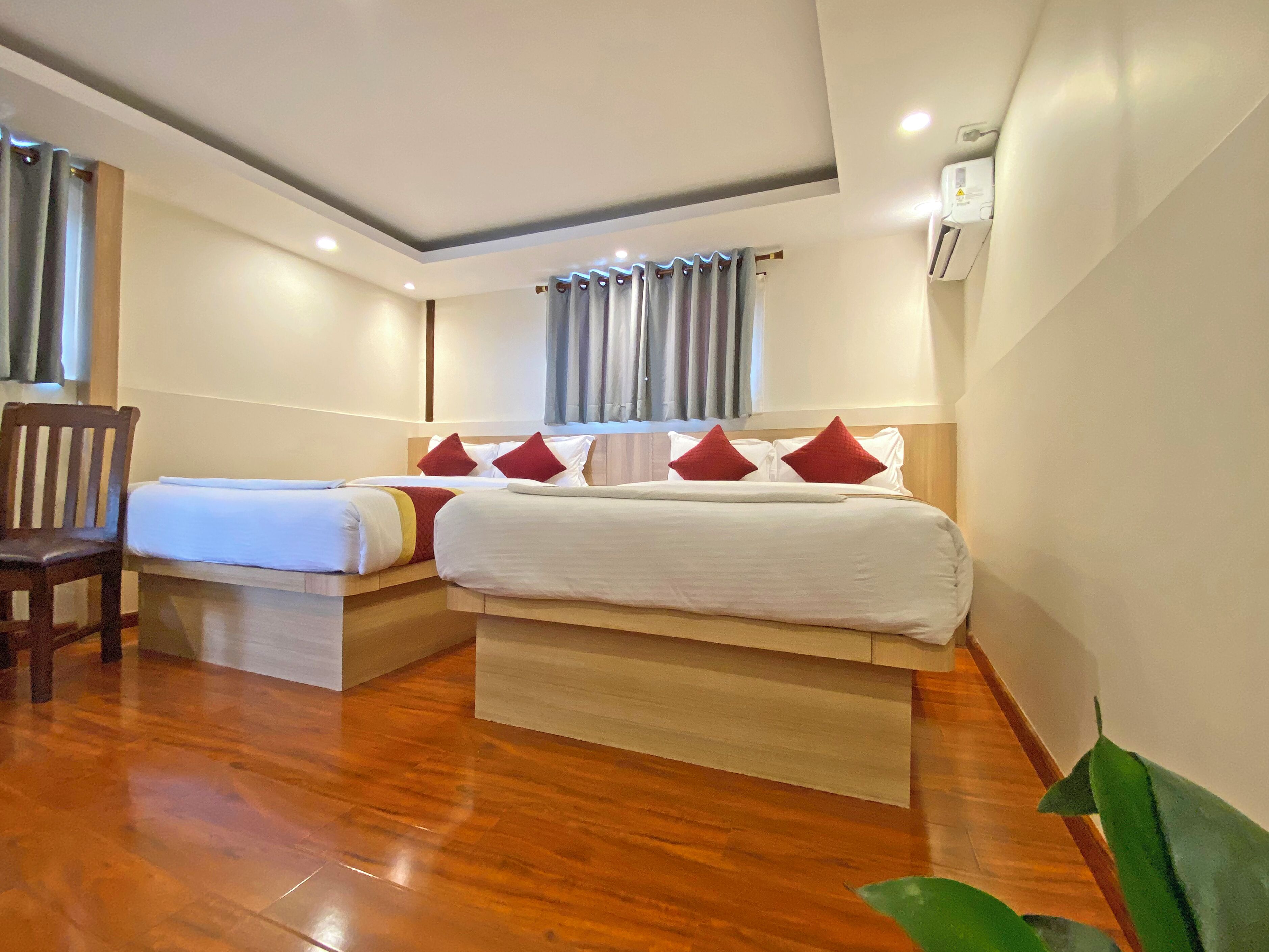 Une chambre d’hôtel avec un plancher en bois, un lit avec une literie blanche et des oreillers rouges, une chaise en bois et une fenêtre avec des rideaux.