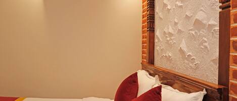 Habitación de hotel con una cama, almohadas rojas y blancas, una pared de ladrillo y un equipo de aire acondicionado.