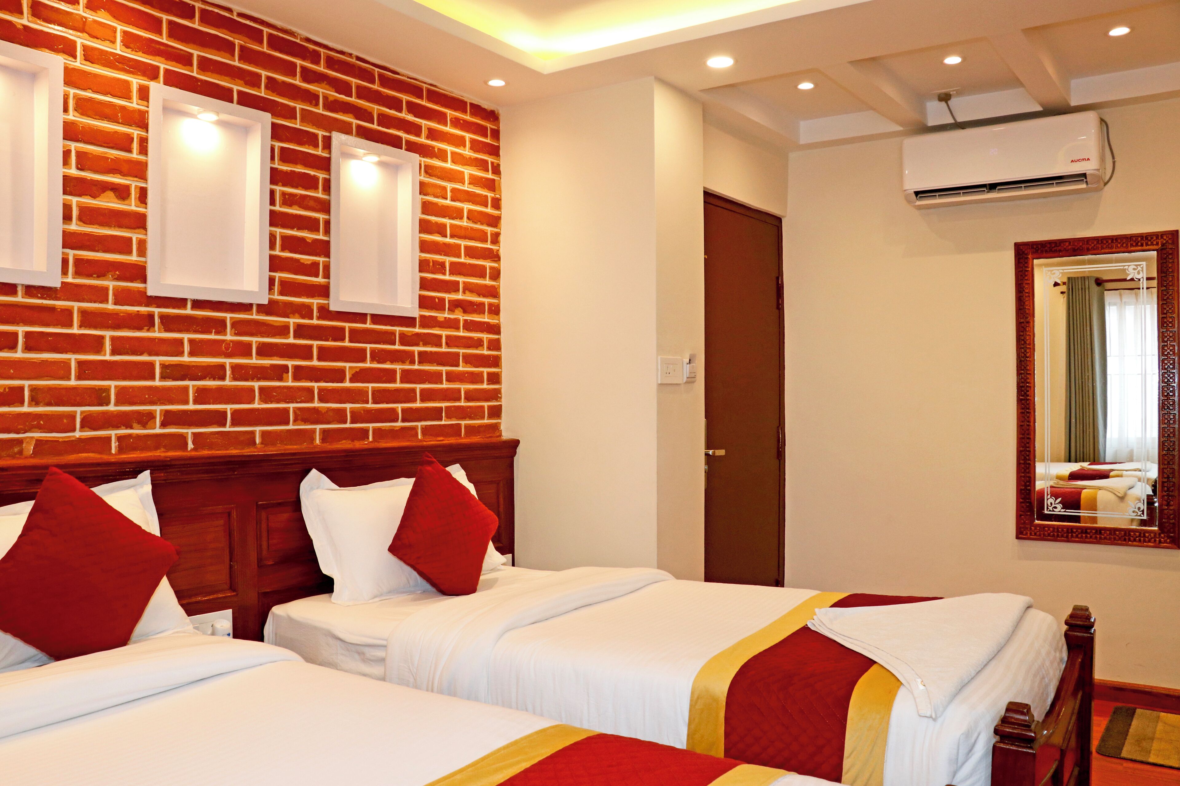 Habitación de hotel con tres camas, una pared de ladrillo y un espejo grande.