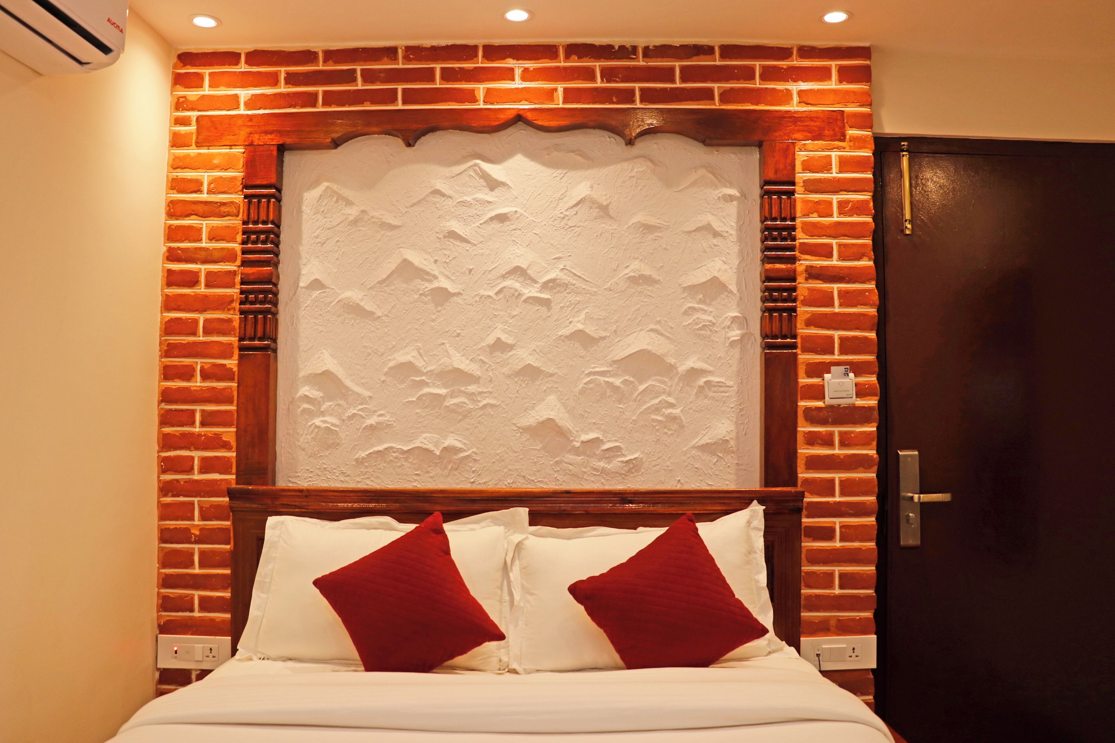 A hotel room with a brick wall, a decorative headboard, and a dark wooden door.