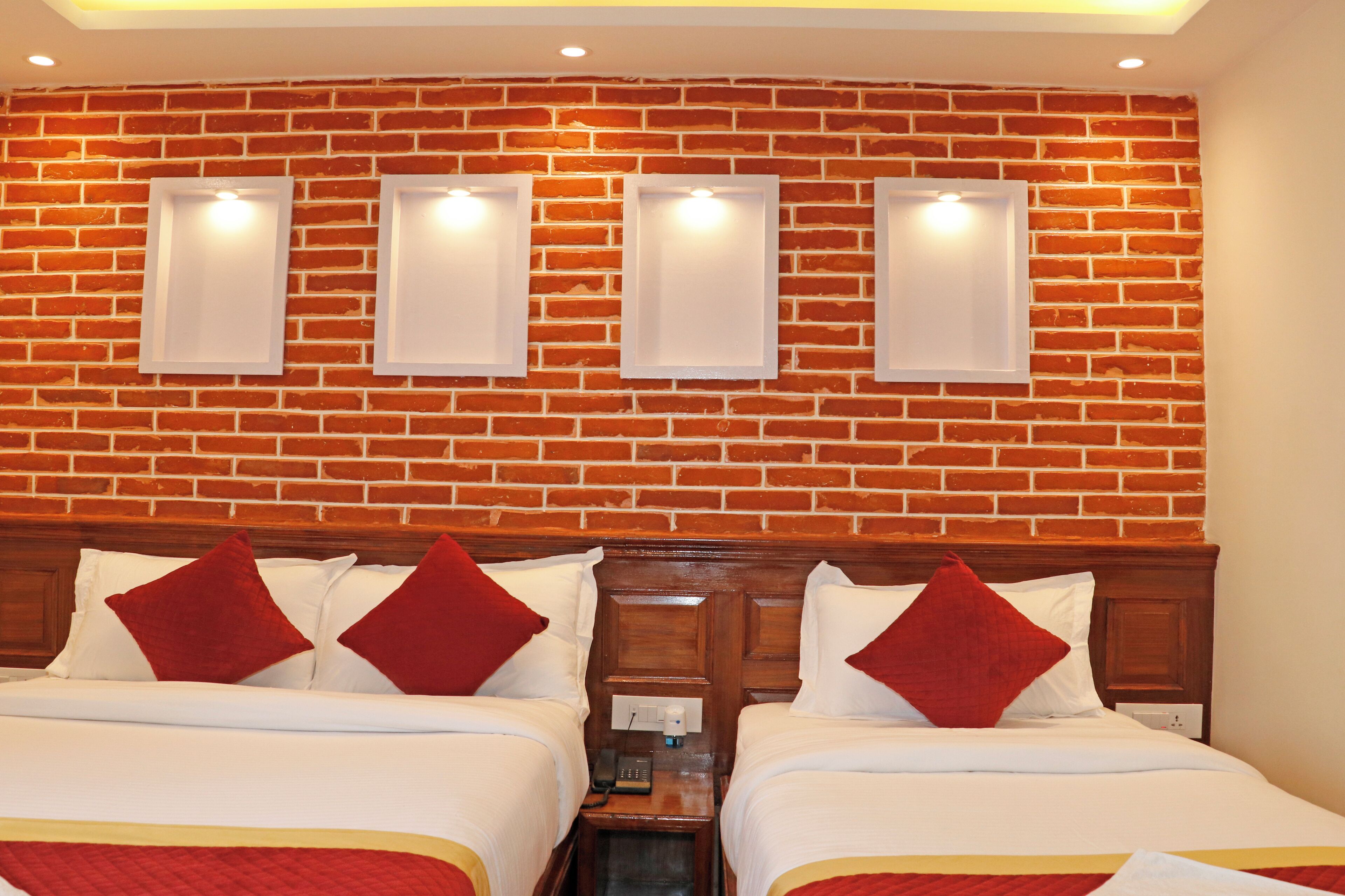 Quarto de hotel com duas camas, uma parede de tijolos e três luminárias fixadas na parede.