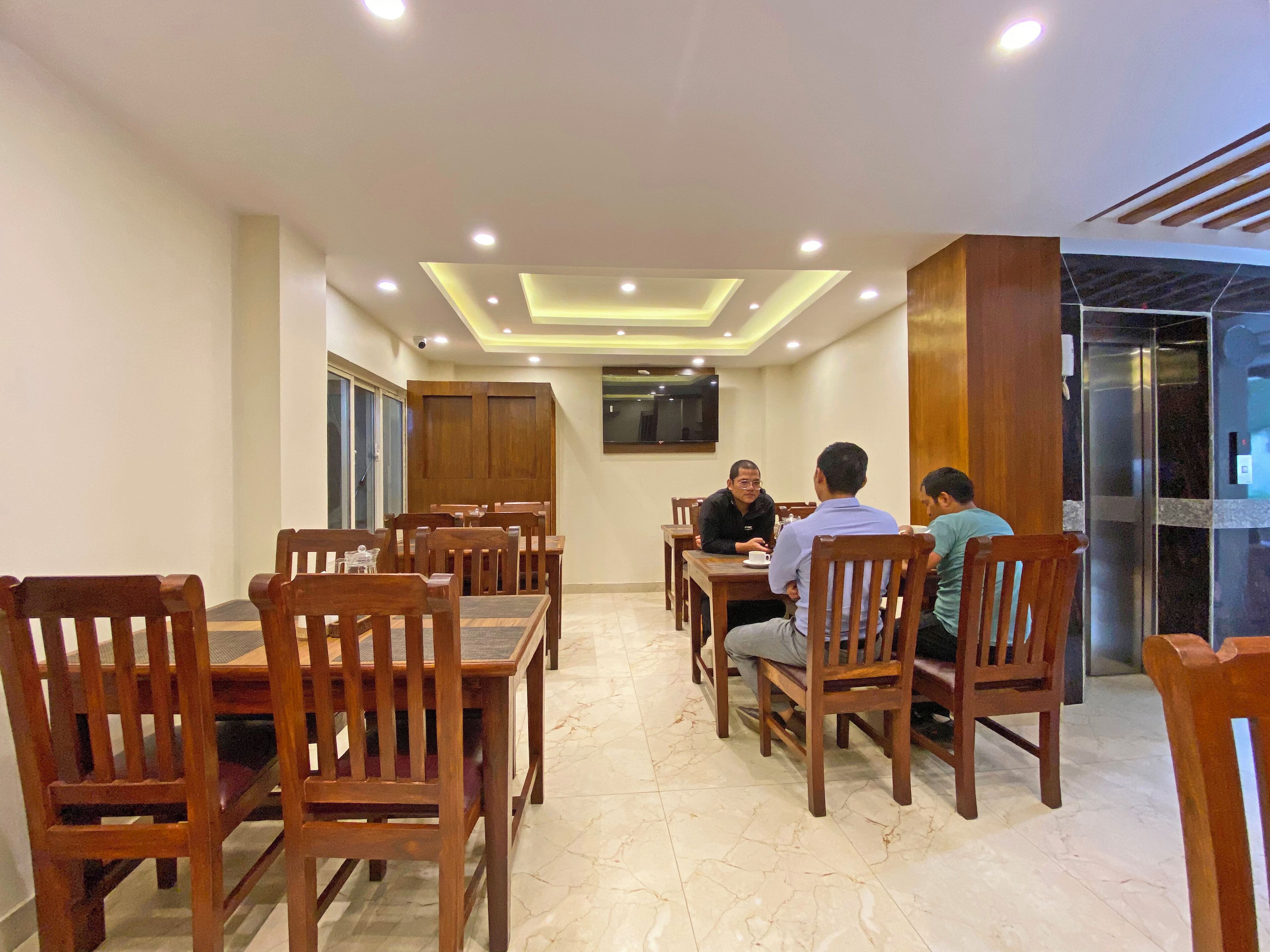A dining area with wooden tables and chairs, recessed ceiling lighting, and a large wooden cabinet.