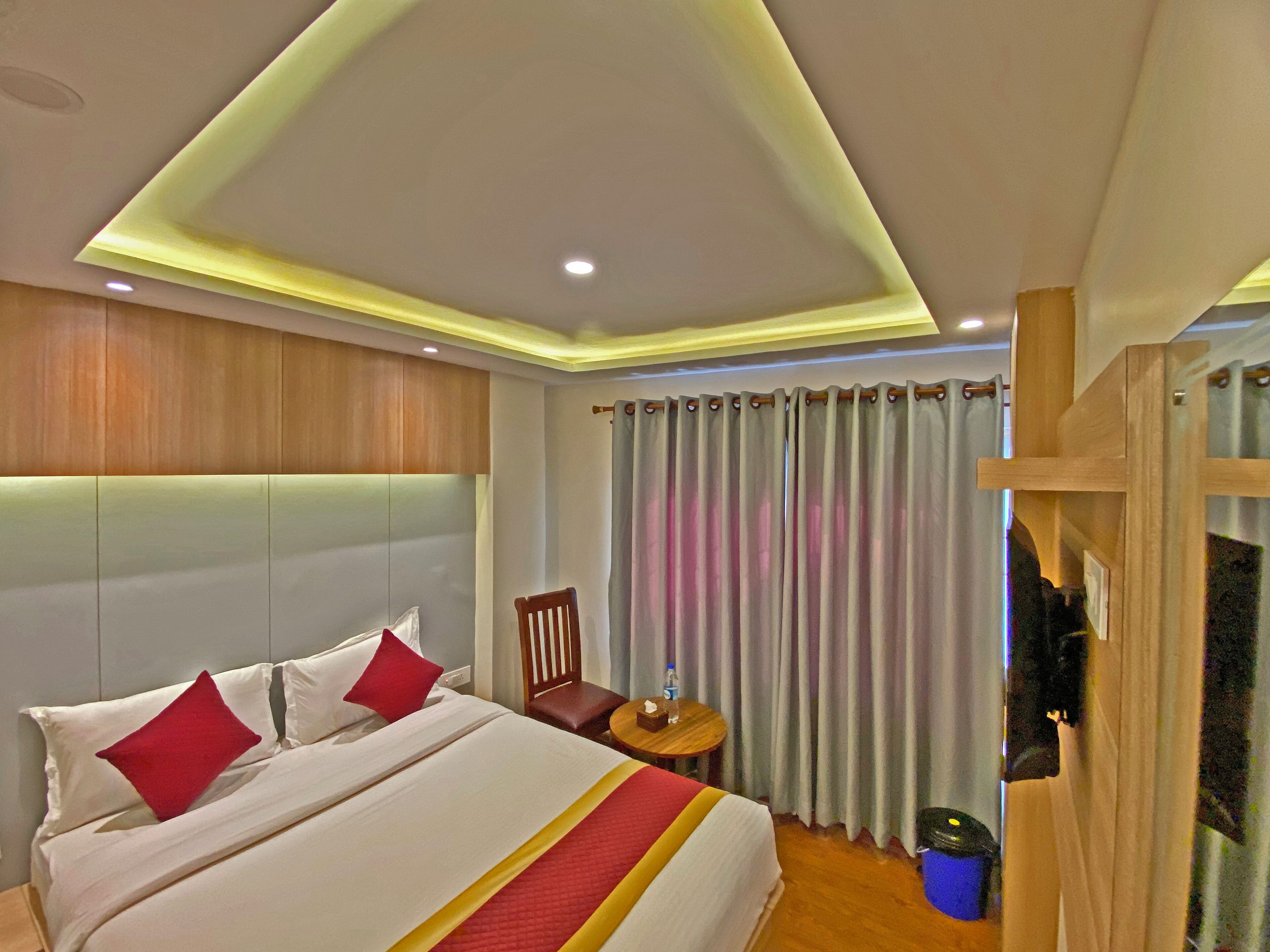 A hotel room with a bed, a chair, a small table, and a curtain.