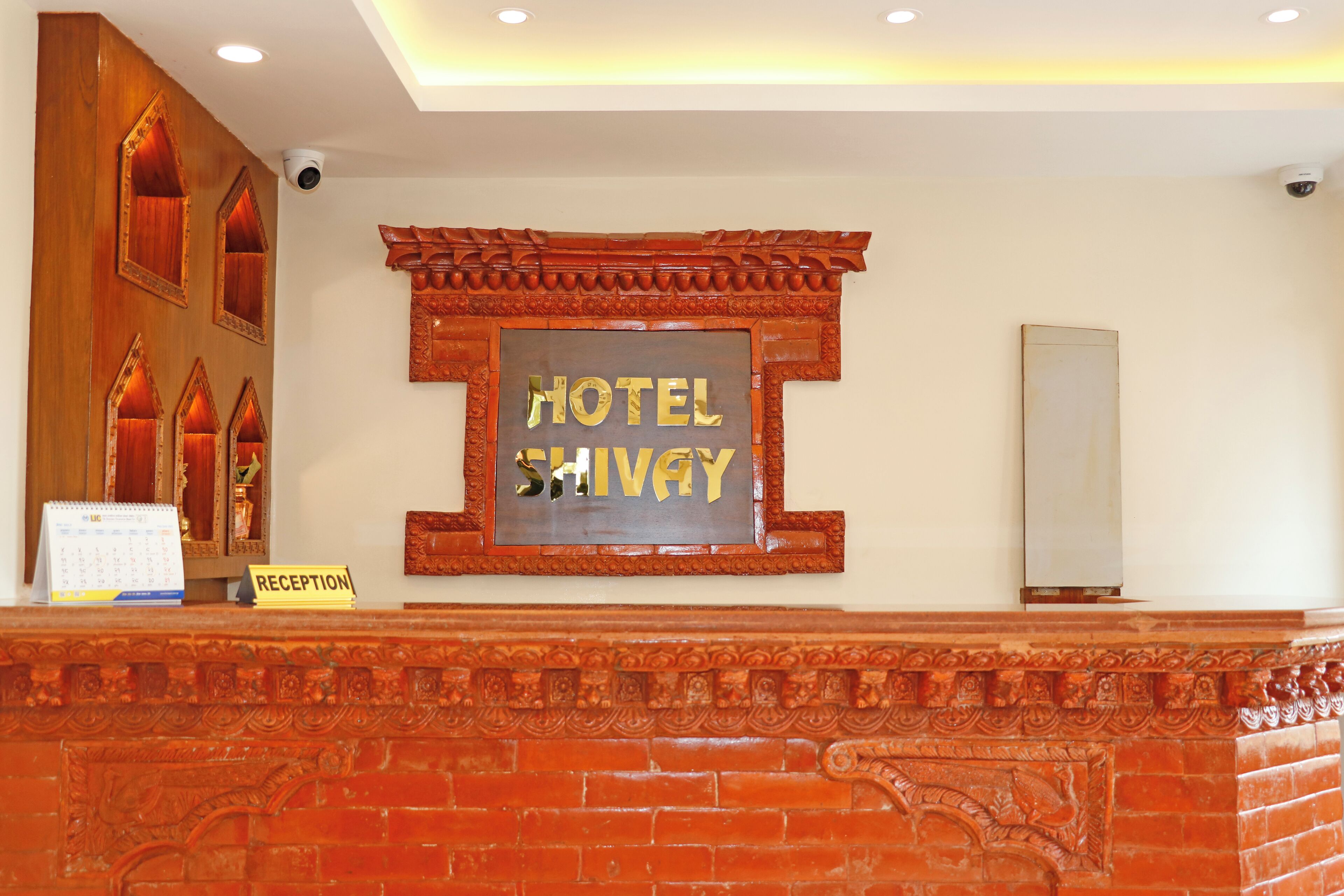 A reception area with a wooden reception desk, a 'HOTEL SHIVAY' sign, and a 'RECEPTION' sign.