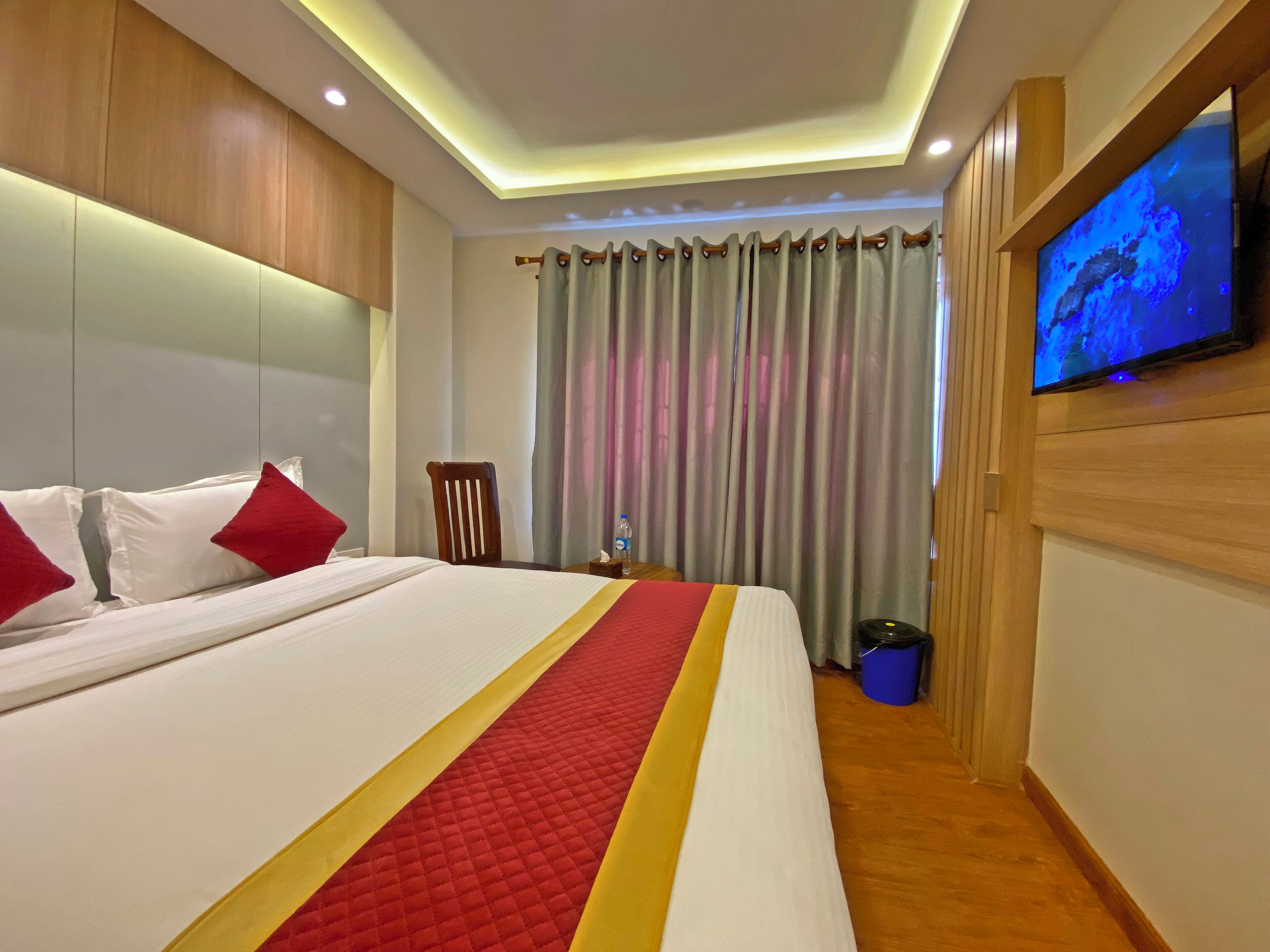 Une chambre d’hôtel avec un grand lit, un téléviseur fixé au mur et un rideau.