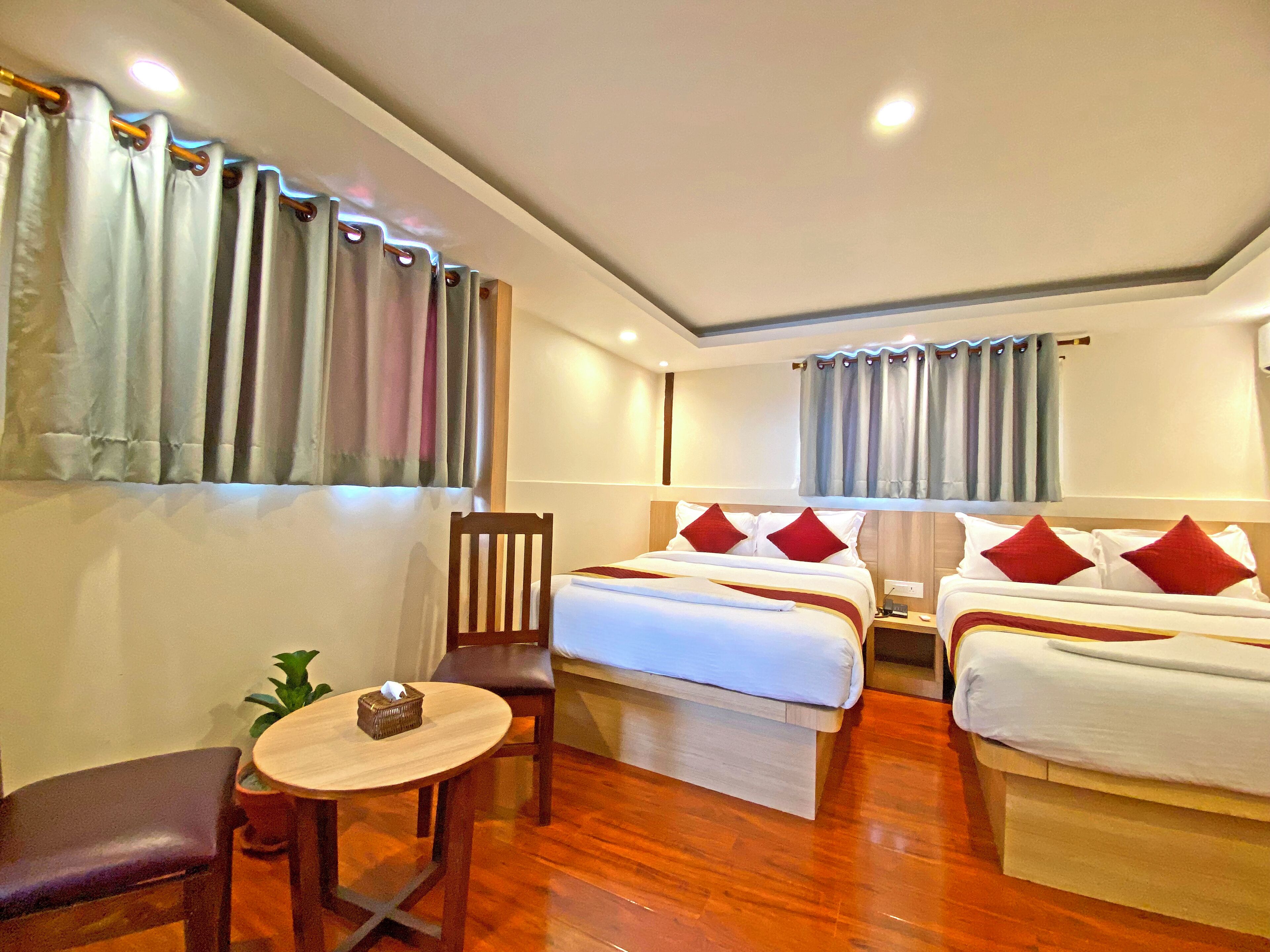A hotel room with two beds, a small table, a chair, and a potted plant.