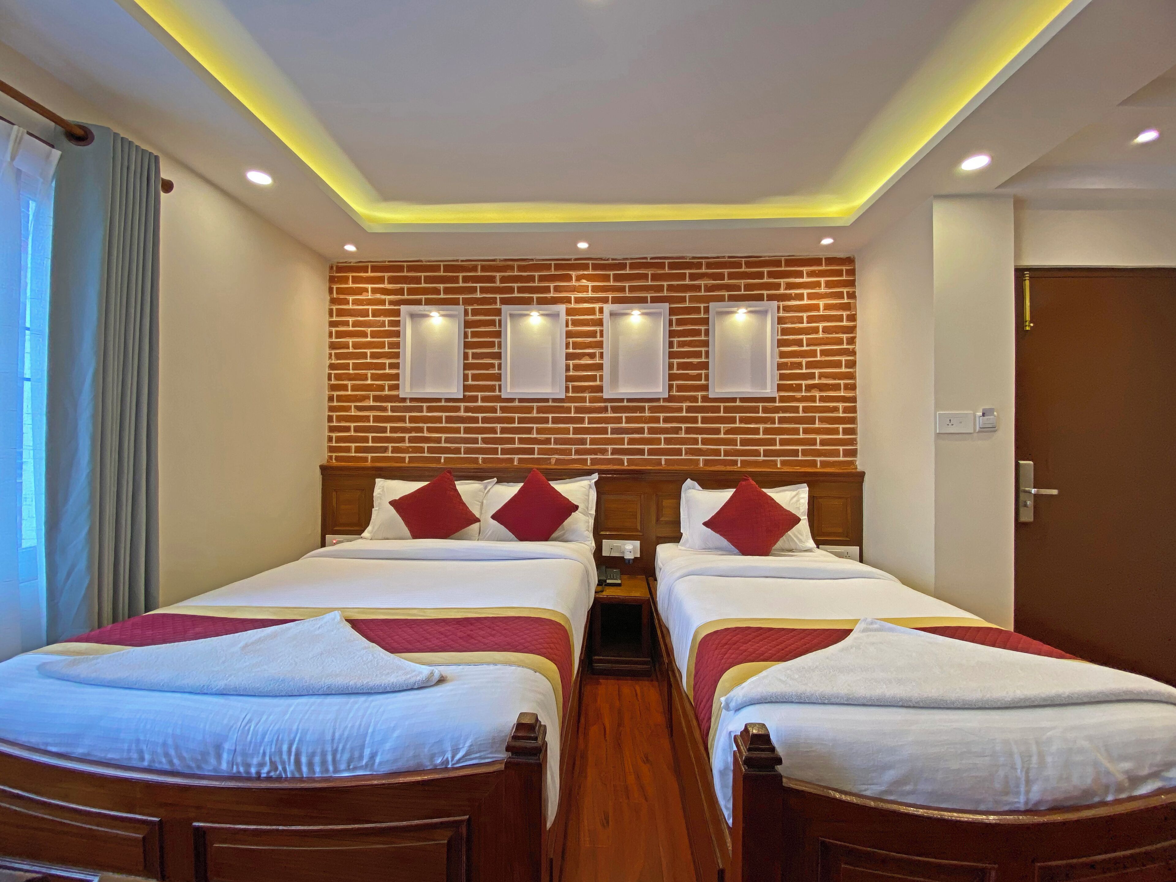 A hotel room with two beds, a brick wall, recessed lighting, and a wooden headboard.