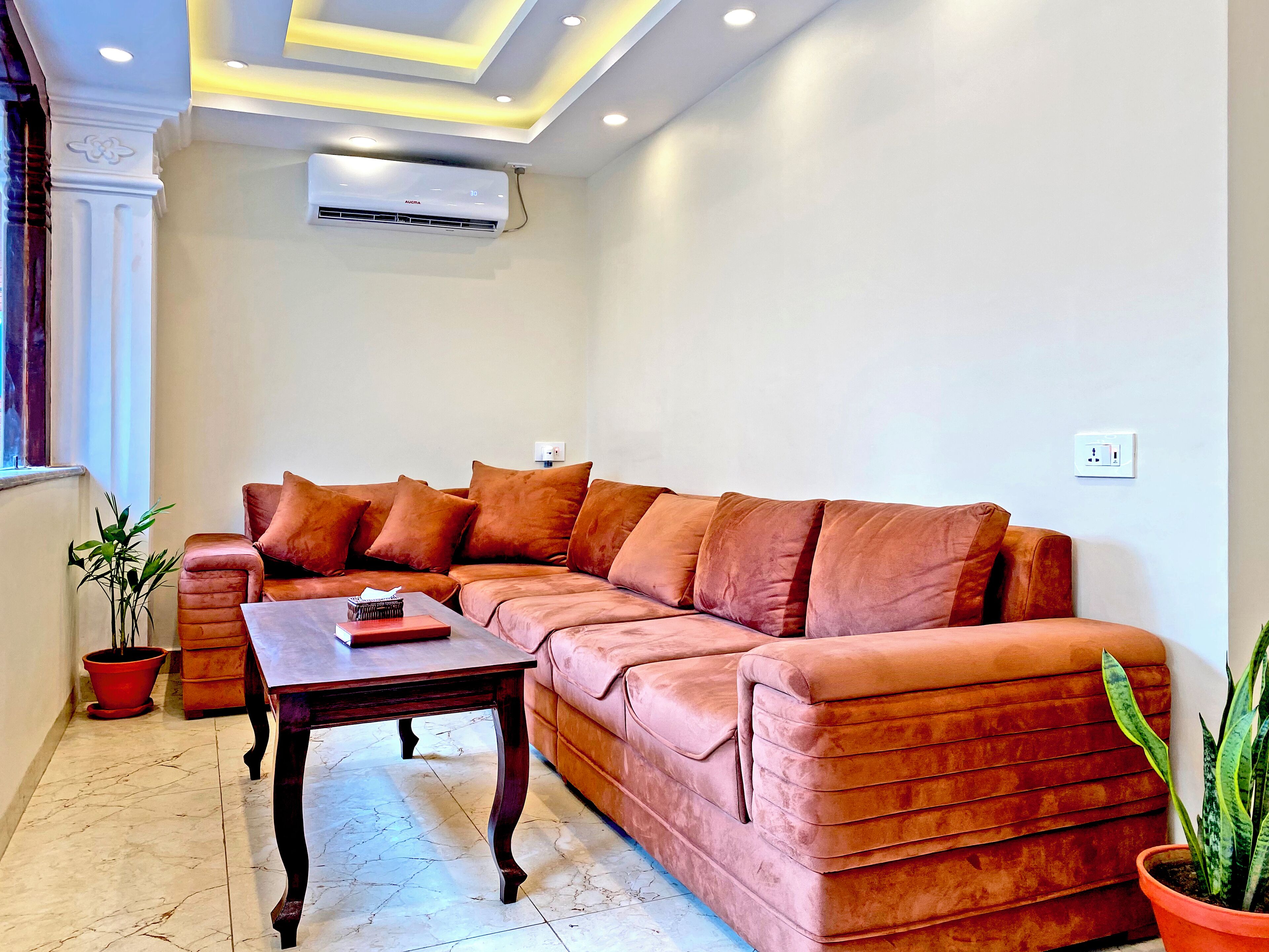A living room with a large sectional sofa, a wooden coffee table, and a potted plant.