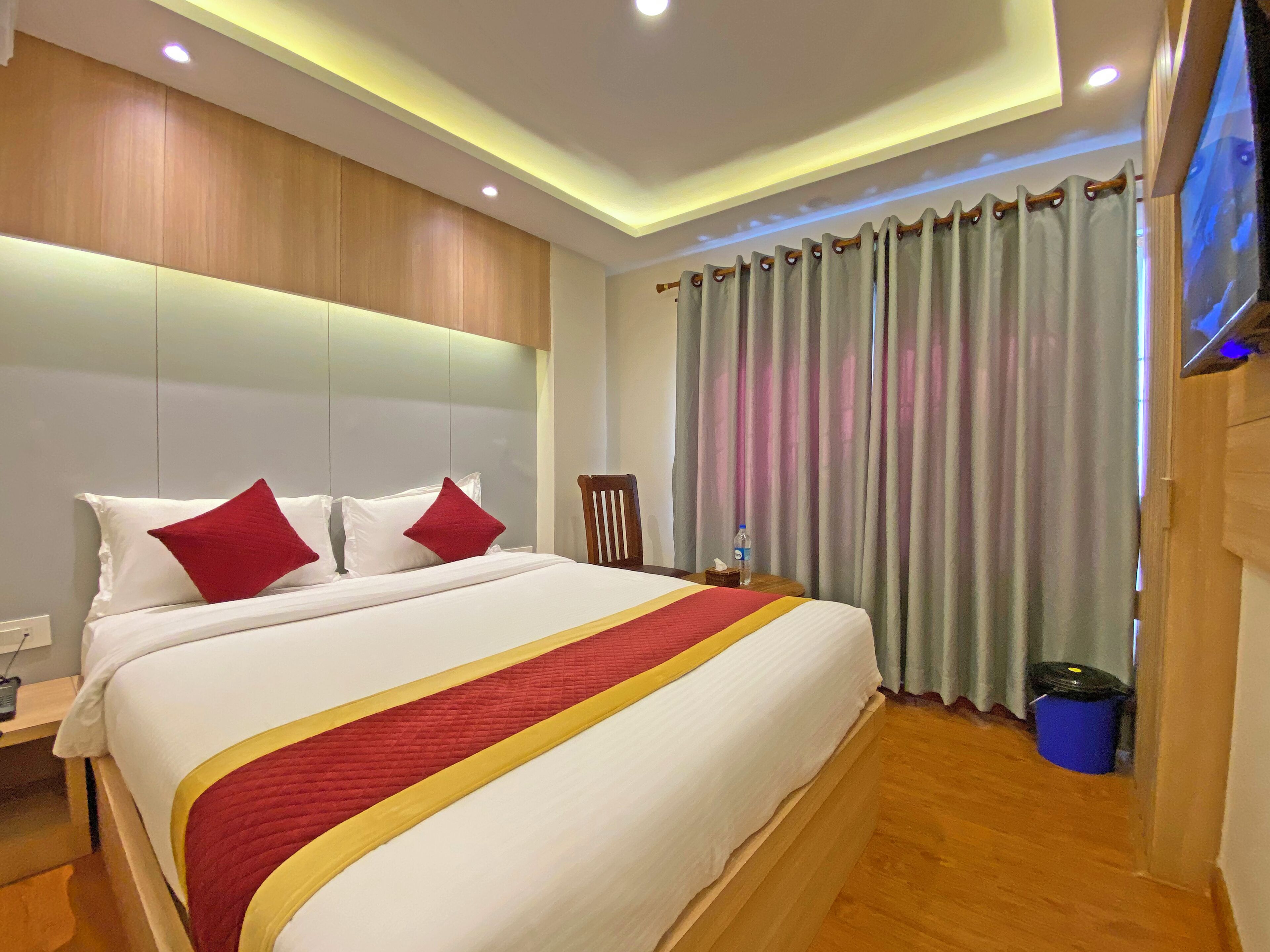 Quarto de hotel com cama grande, cabeceira de madeira e televisão fixada na parede.