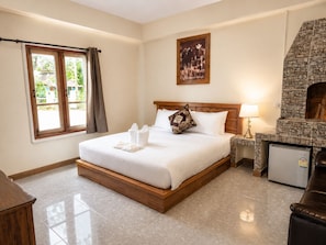 A hotel room with a bed, a stone fireplace, a window with curtains, and a small refrigerator.