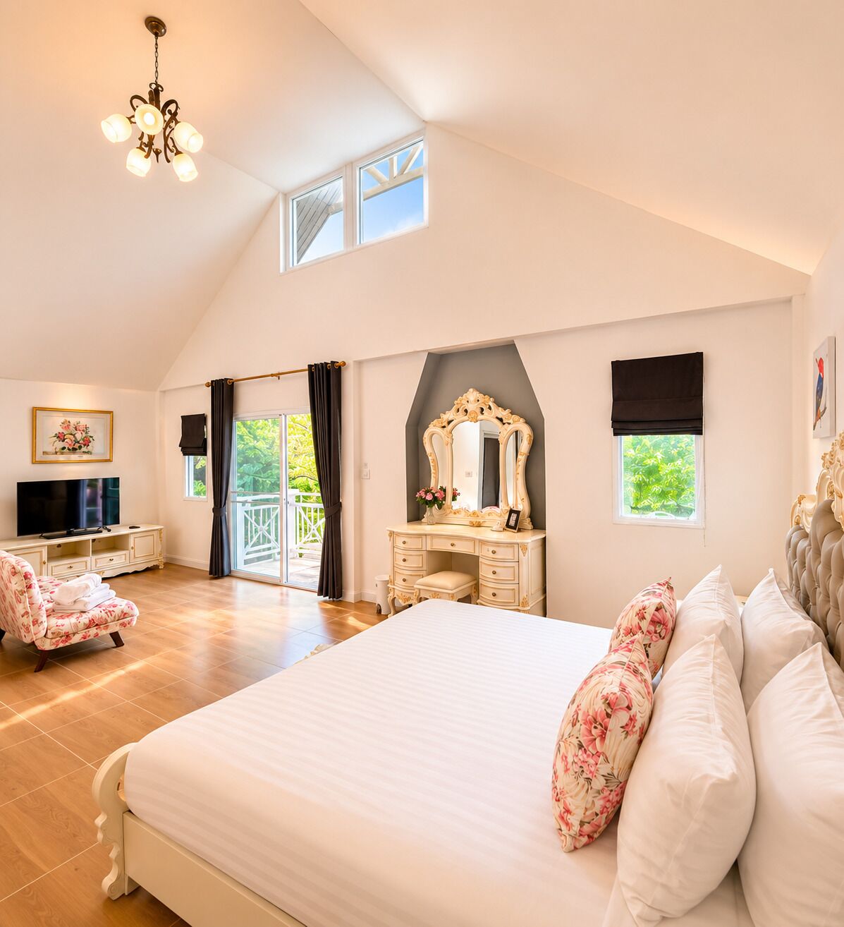 A spacious bedroom with a large bed, a vanity with a mirror, a television, and a balcony with curtains.
