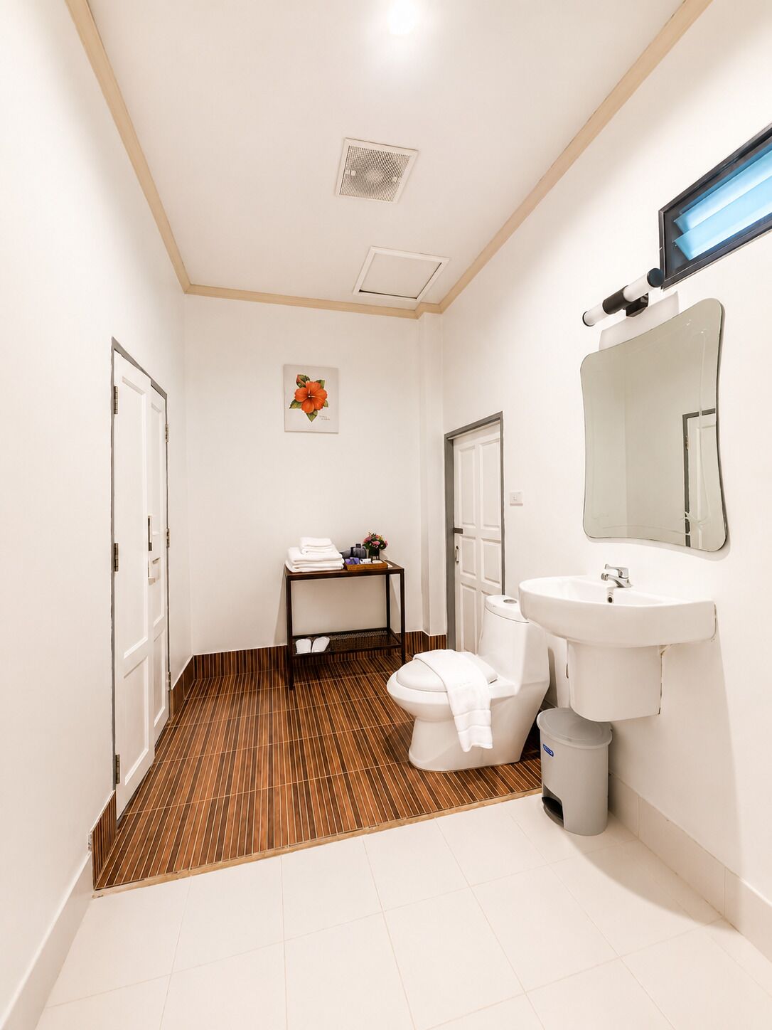 A bathroom with a toilet, sink, mirror, and a small table with towels.