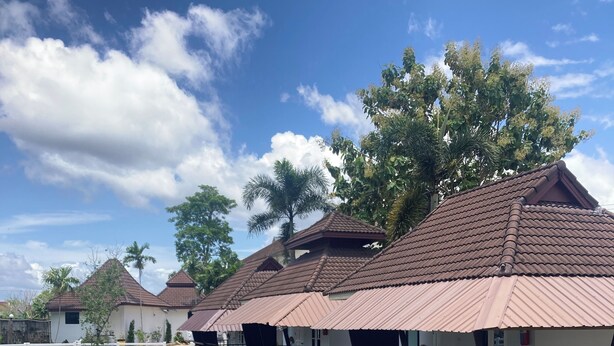A row of traditional-style buildings with tiled roofs, surrounded by water, and palm trees in the background.