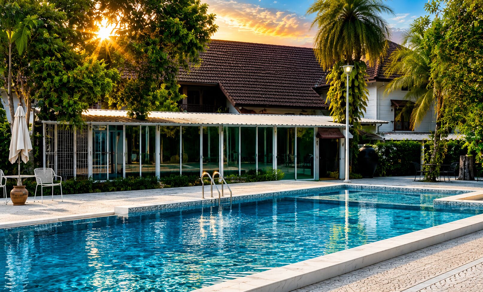 Una piscina con zona cubierta, rodeada de árboles y un edificio de tejado con baldosas.