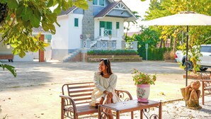 A woman sitting on a bench in a courtyard with a house in the background.