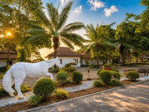 A white horse statue in a landscaped garden with palm trees and a building in the background.
