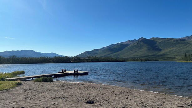 A lake with a wooden dock and benches, surrounded by mountains and clear skies. - 
Denali Haven: A Cosy Alaskan Retreat near Denali NP (Healy)