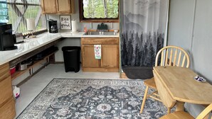 A compact kitchen with wooden cabinets, a coffee maker, a toaster, and a sink. There's a rug on the floor and a chair near the table. - 
Denali Haven: A Cosy Alaskan Retreat near Denali NP (Healy)