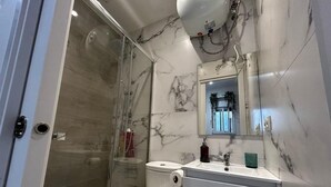 A modern bathroom with a glass-enclosed shower, a white toilet, and a marble backsplash.