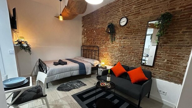 A compact bedroom with a bed, a sofa, a small table, and a mirror.