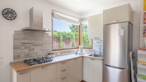 A modern kitchen with a gas stove, stainless steel refrigerator, and a window with a view of greenery.