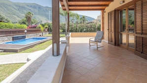 A covered outdoor area with a pool, a chair, and a view of mountains.