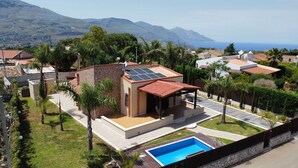 A residential area with a house featuring a swimming pool, solar panels, and a view of the sea.