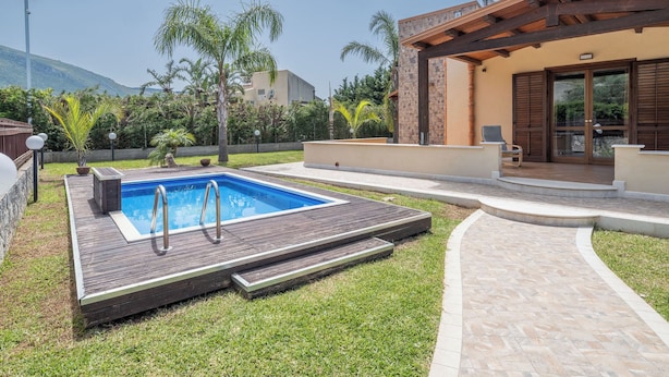 A swimming pool with a wooden deck, surrounded by a well-maintained lawn and palm trees.