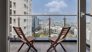 A balcony with two wooden chairs and a view of a cityscape through a glass railing.