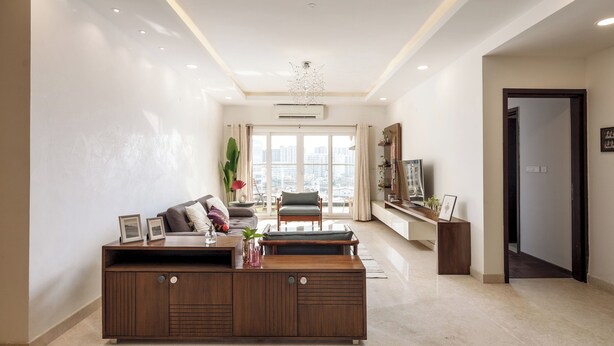A modern living room with a large wooden entertainment unit, a sofa, and a coffee table. There is a large window with a view of the city.