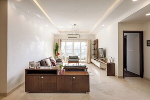 A modern living room with a large wooden entertainment unit, a sofa, and a coffee table. There is a large window with a view of the city. - The Ivy Apartment by Red Olive (Hyderabad)