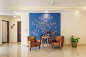 A lobby with two leather armchairs, a small table with a vase, and a large blue floral mural on the wall. - The Ivy Apartment by Red Olive (Hyderabad)
