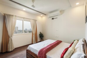 Quarto com cama, cortinas, planta em vaso e ar condicionado.