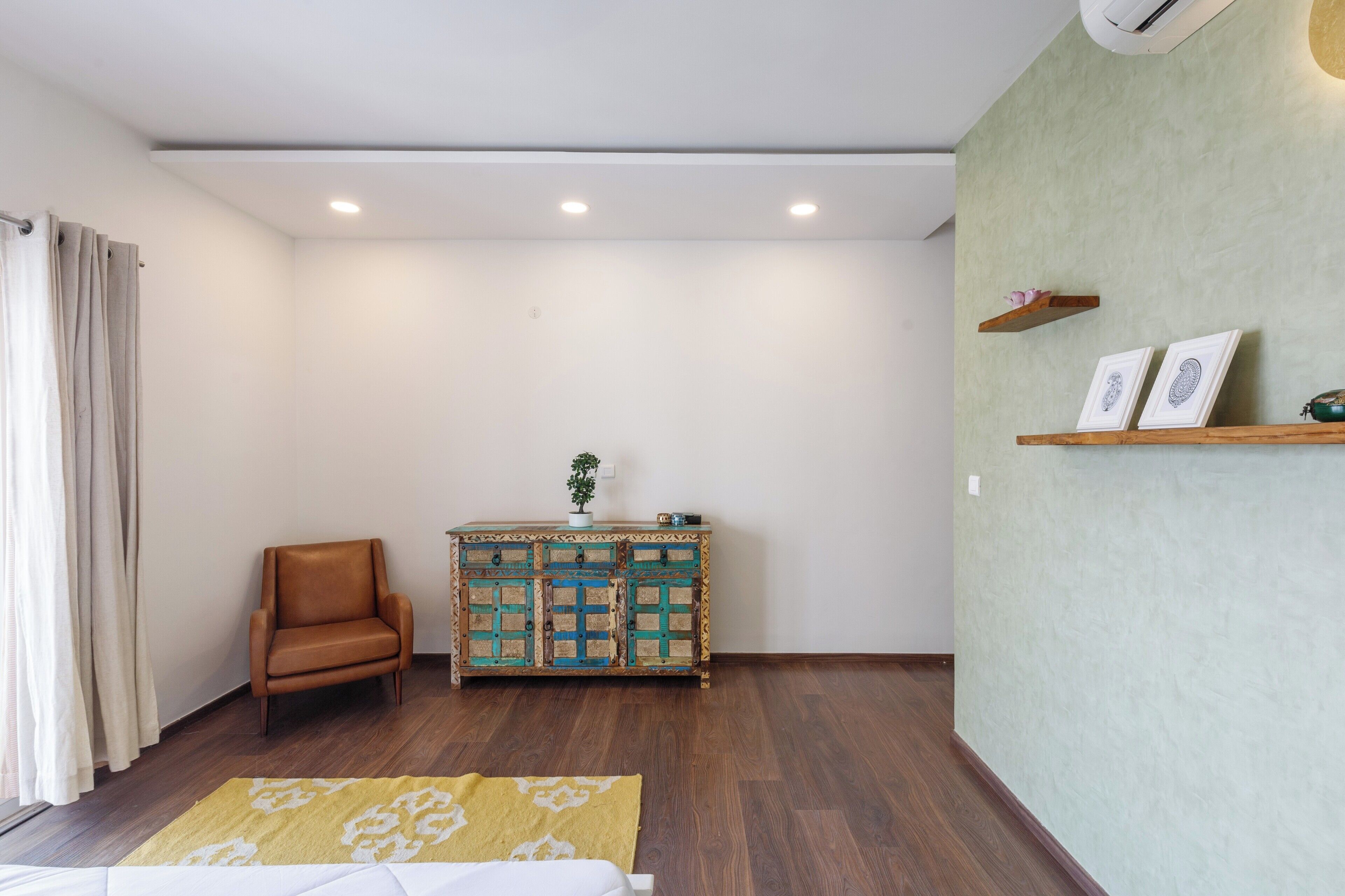 Een kamer met een bruine leren fauteuil, een houten kast met decoratieve panelen, een geel gekleurd vloerkleed en een groene, gestructureerde muur.