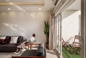 Uma sala de estar moderna com um sofá, uma mesinha e uma cadeira. Há uma janela grande com cortinas e vista para o exterior.