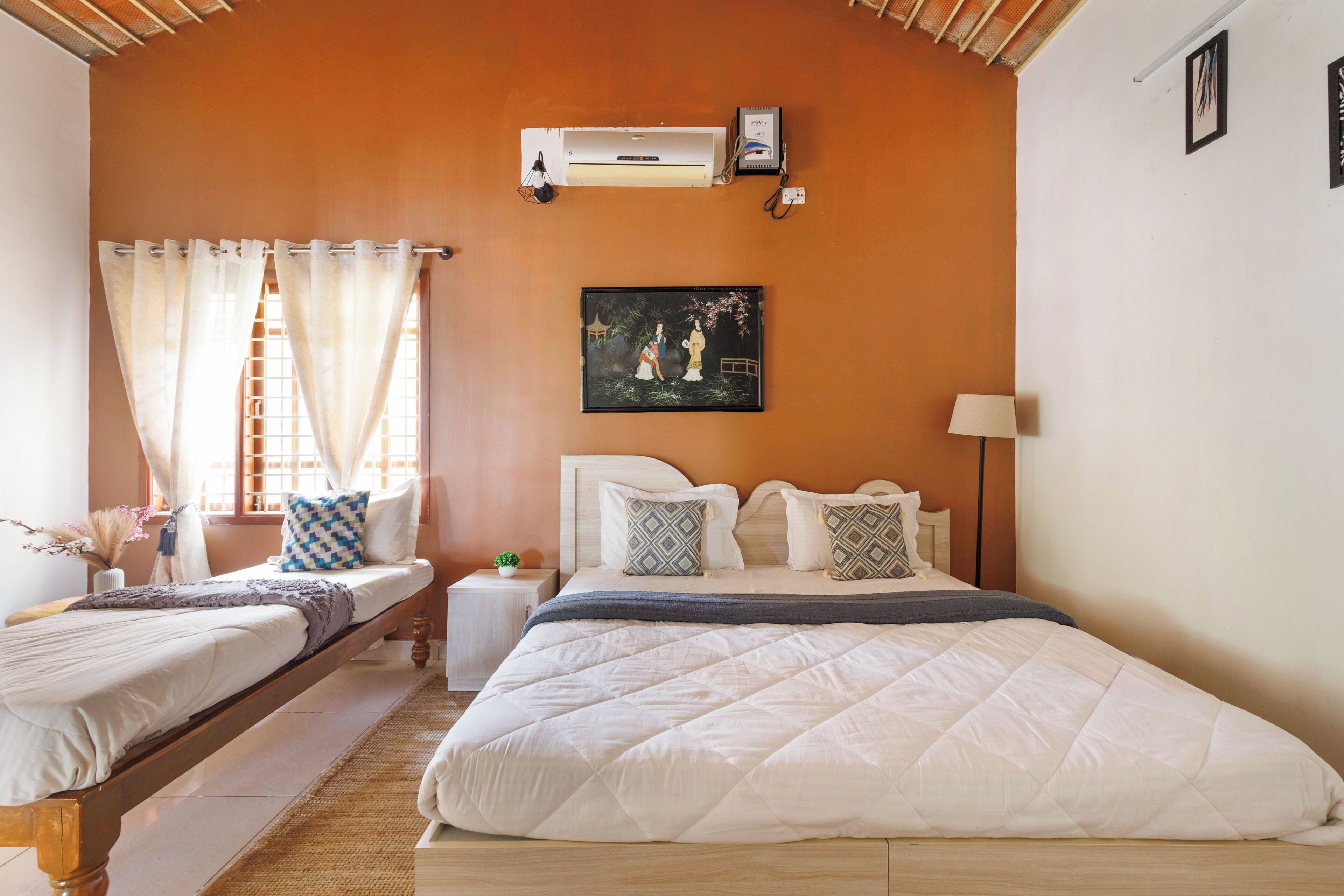 A bedroom with a large bed, a smaller bed, a nightstand, an air conditioner, and a painting on the wall.
