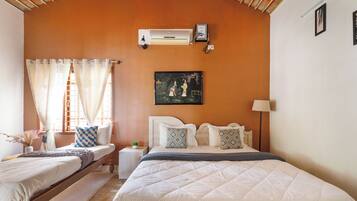 A bedroom with a large bed, a smaller bed, a nightstand, an air conditioner, and a painting on the wall.