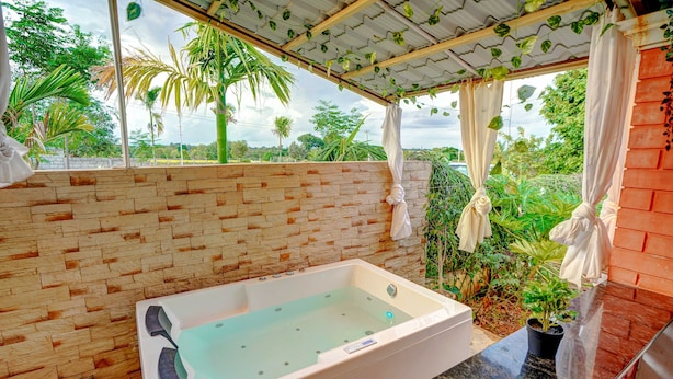 A spa area with a large bathtub, a stone wall, and a view of lush greenery. - Rosedale Farmhouse (Denkanikota)