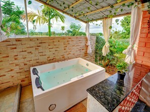 A spa area with a large bathtub, a stone wall, and a view of lush greenery. - Rosedale Farmhouse (Denkanikota)