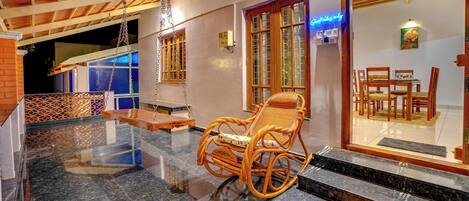 A wooden rocking chair on a marble floor, a 'WELCOME' mat, and a view into a dining area with wooden furniture.