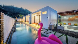 Een modern huis met een zwembad, een roze flamingo en een terras met zitplaatsen.