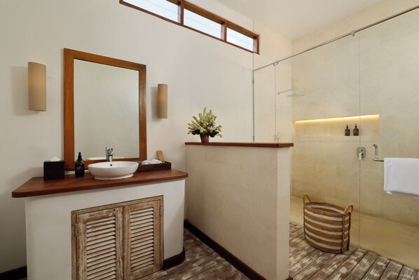 Un baño moderno con un tocador de madera, un espejo grande, un lavabo y una zona de ducha, además de una pequeña cesta.