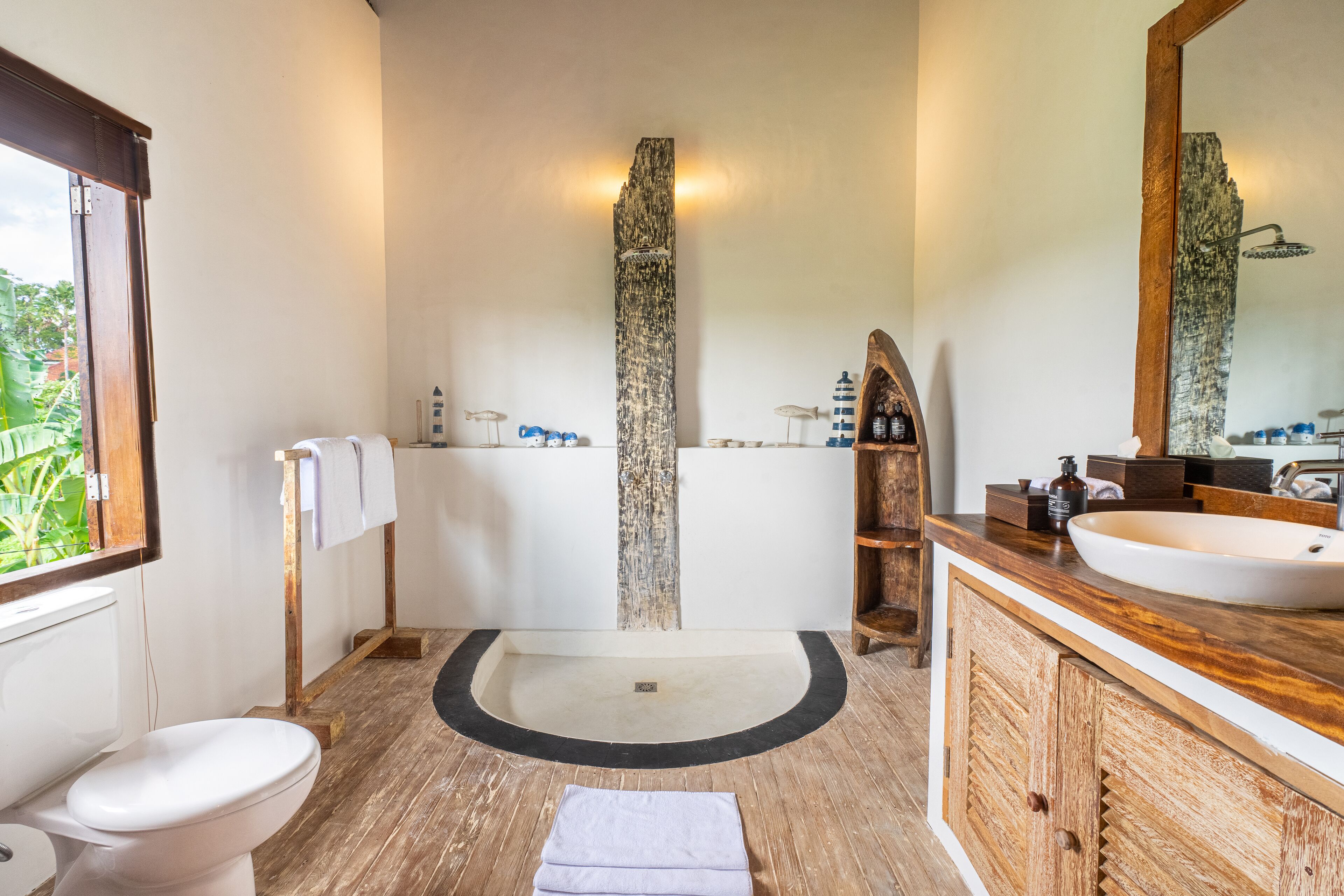 A bathroom with a wooden vanity, a large mirror, a white sink, and a shower area.