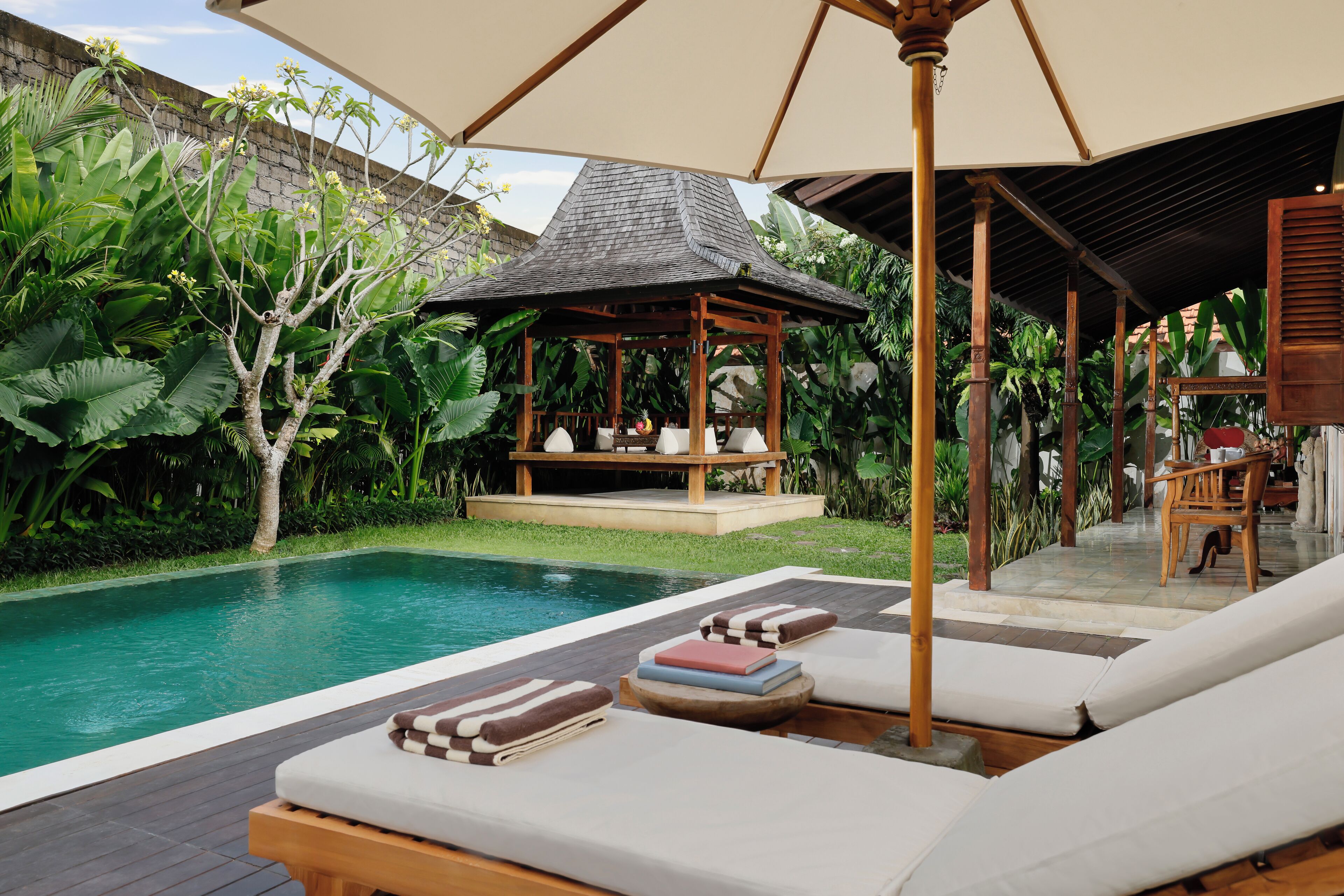 A poolside area with lounge chairs, a wooden gazebo, and lush greenery.
