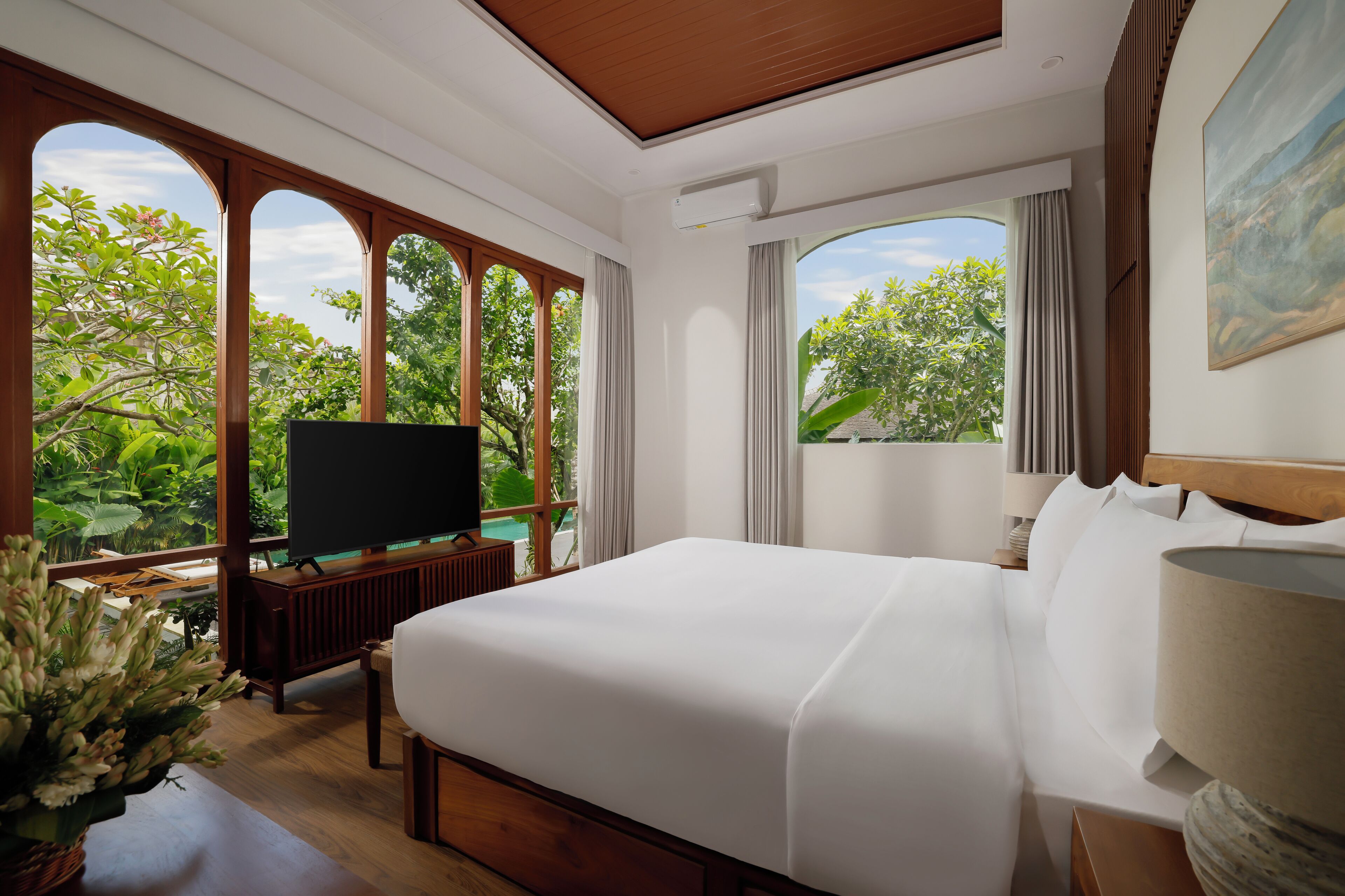 A hotel room with a large bed, a TV, and a view of lush greenery.